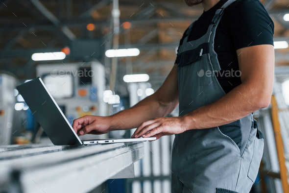 Typing on keyboard. Industrial worker indoors in factory. Young technician with orange hard hat