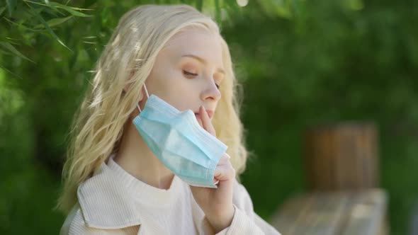 Young Beautiful Blonde Woman Takes Off a Medical Mask and Sniffs a Yellow Dandelion