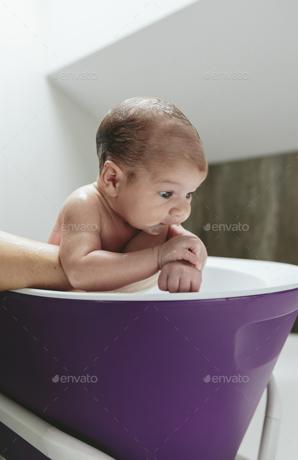 Newborn in the bathtub held by her mother Stock Photo by davidpereiras