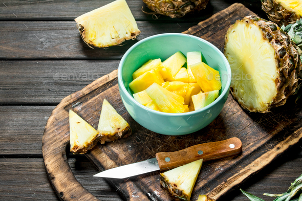 Sliced pineapple in a bowl on a cutting Board with a knife and a whole  pineapple. Stock Photo by Artem_ka2