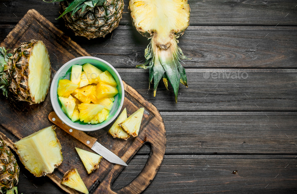 Sliced pineapple in a bowl on a cutting Board with a knife and a whole  pineapple. Stock Photo by Artem_ka2