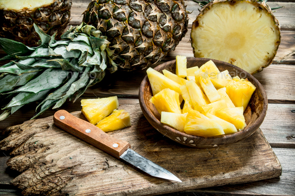 Sliced pineapple in a bowl on a cutting Board with a knife and a whole  pineapple. Stock Photo by Artem_ka2