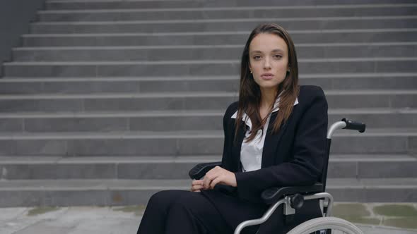 Portrait of Handicapped Serious Businesswoman in Suit Sitting in Wheelchair at Street alt