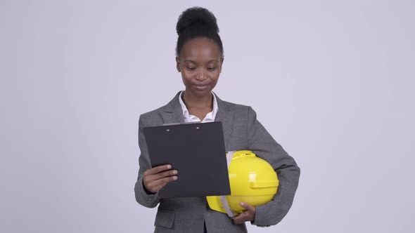Young Happy African Businesswoman Holding Hardhat While Reading on Clipboard alt