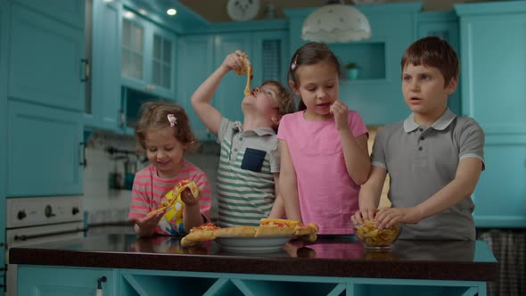 Two boys and two girls enjoy eating pizza with hands at home 