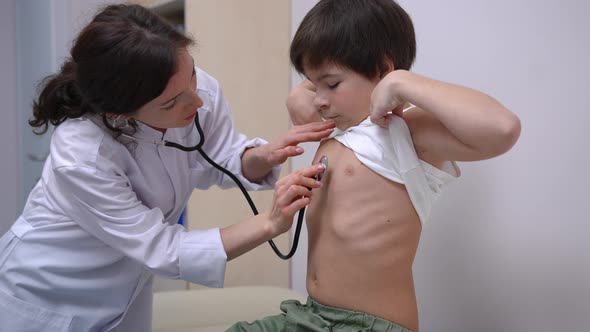 Caucasian Ill Boy Raising Tshirt As Doctor Listening Auscultation in Hospital alt