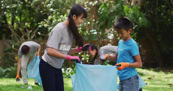 Smiling asian brother and sister holding refuse sack, collecting plastic waste and high fiving alt