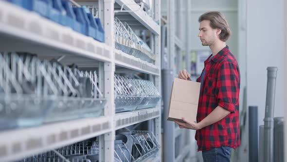 Focused Handsome Young Man Putting Pipe Connectors in Disposable Paper Bag and Leaving alt