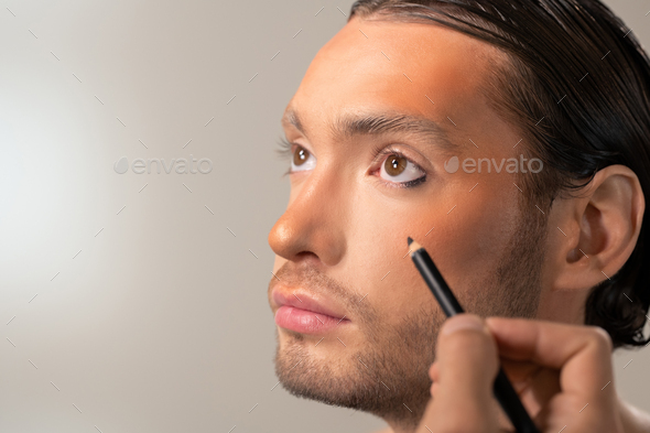 Hand of young makeup artist with black kohl eye liner going to apply it