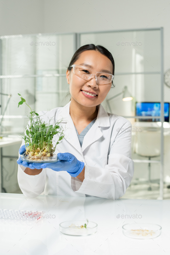 Happy laboratory worker holding petri dish with green lab-grown soy sprouts