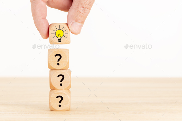 Hand picked wooden cube block with question mark symbol and light bulb icon