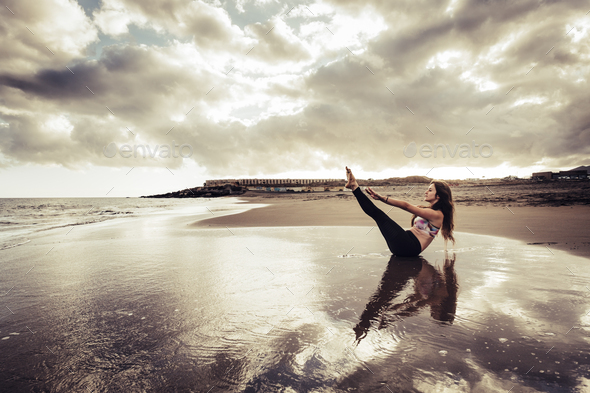 Nice girl have balance pilates workout exercise at the beach on the shore with sea and sunset