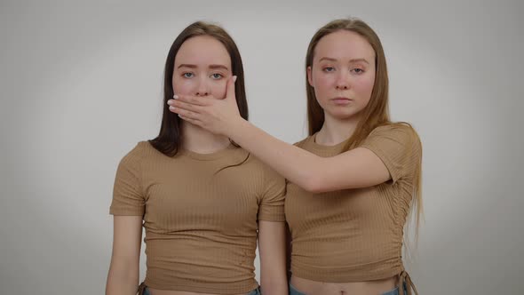 Front View Identical Twin Sisters Closing Mouth and Eyes of Each Other with Hand alt