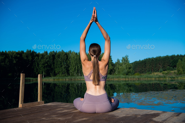 Beautiful young woman performing a spiritual yoga pose on a forest lake at sunny day, sunrise zen