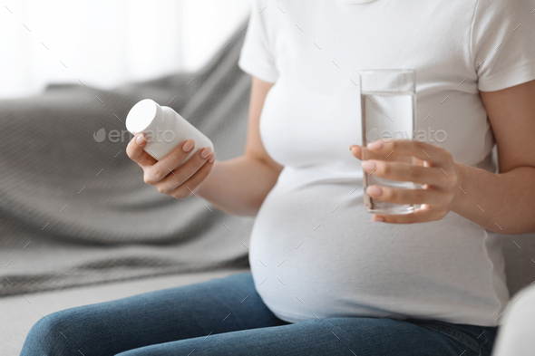 Prenatal Vitamins. Pregnant woman holding jar with supplements and glass of water