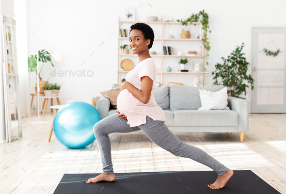 Sporty African American woman stretching her leg on yoga mat at home Stock  Photo by Prostock-studio