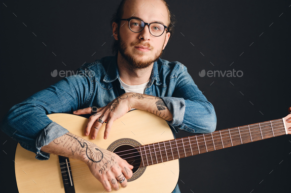 Young attractive tattooed man looking confident posing with guitar. Stylish musician with guitar