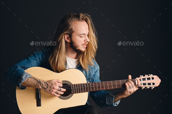 Tattooed guy with long hair playing guitar singing preparing for concert.  Stylish singer with guitar Stock Photo by garetsworkshop