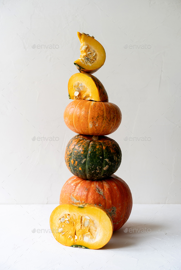 High long pyramid of a variety of whole and pieces of pumpkins on a white concrete background