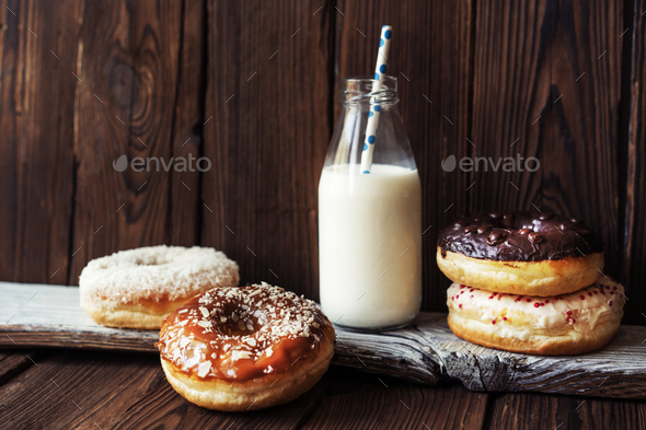 Several donuts and milk in a bottle with a straw on a dark wooden textured rustic background.