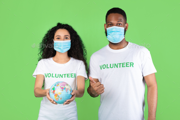 Volunteers Wearing Masks Holding Globe Posing Gesturing Thumbs-Up, Green Background