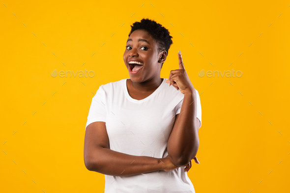 Cheerful Overweight Black Woman Pointing Finger Having Idea, Yellow Background