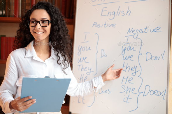 Smiling female teacher pointing at whiteboard, explaining rules