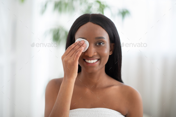 Cheerful african american lady cleanses skin with cotton pad and cosmetics product for properly deep