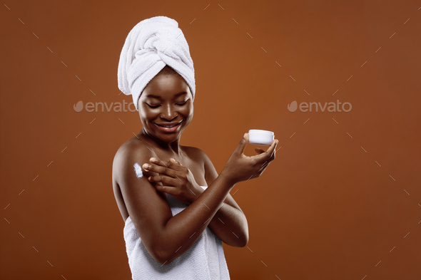 Skin Care Products. African Lady With Towel On Head Applying Body Cream