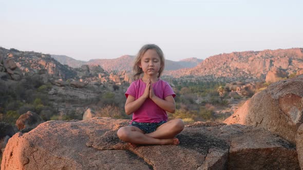 Little Cute Girl Meditating on Top of Mountain