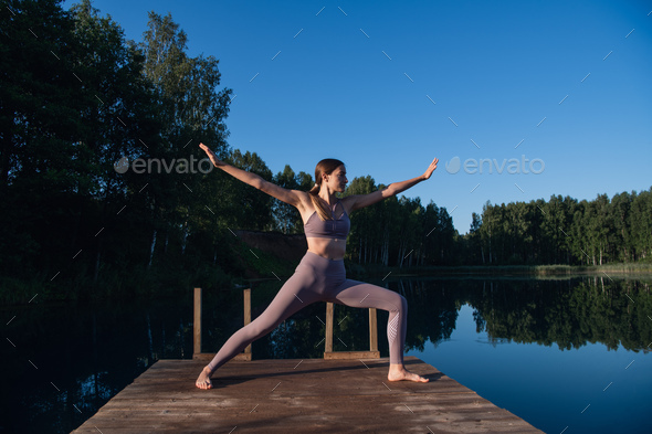 Healthy woman practicing yoga on the lake at sunrise enjoying positive energies from nature