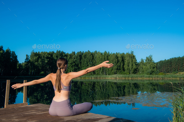 Beautiful young woman performing a spiritual yoga pose on a forest lake at sunny day, sunrise zen