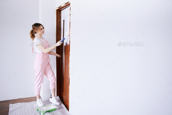A girl in a pink work suit repaints an old door. Renovation and new life for old things.