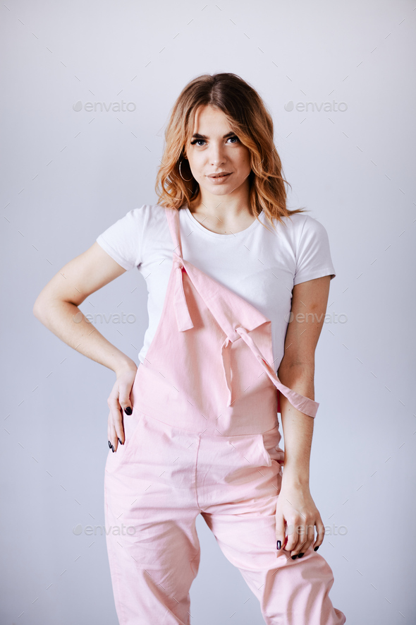 A woman in a pink in work clothes on a gray background is looking at the camera.
