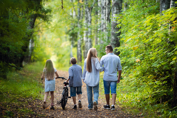 Rear view of family walking along autumn path in a park or forest Stock  Photo by romankosolapov