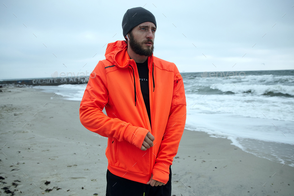 male looking thoughtfully ahaead while fastening zipper on his orange sporty hoodie
