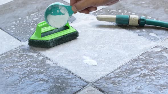 human hand pours detergent onto the wet tile floor to clean it.