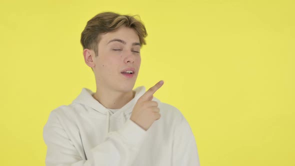 Young Man Pointing Towards Product on Yellow Background alt