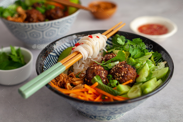 Vietnamese bowl of rice noodles with vegetables and spicy dressing on a white background bun cha