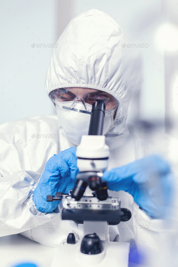 Medical engineer in ppe suit in modern laboratory looking at sample