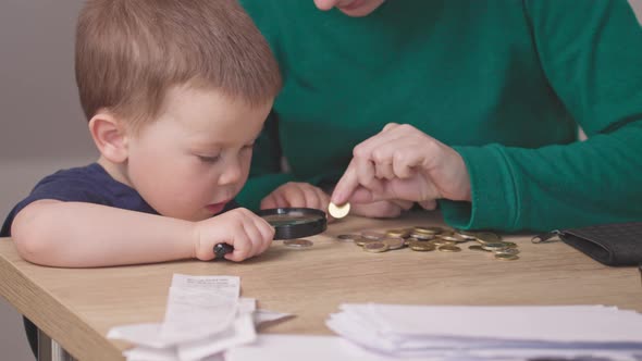 Portrait Baby Boy Kid Looking at Money Coins with Magnifying Glass Hands Helping alt
