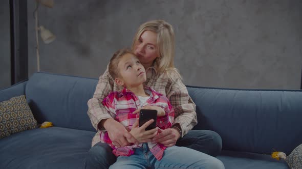Positive Mom with Cute Girl Sharing Smartphone on Couch alt