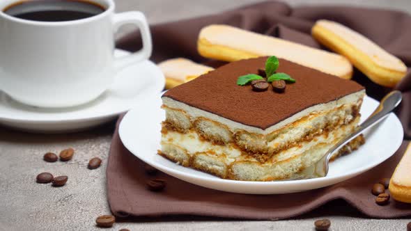 Portion of Traditional Italian Tiramisu dessert and cup of coffee on grey concrete background alt