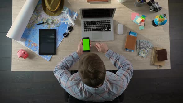 Man Swiping Pages on Smartphone With Green Screen, Using Travel Application alt