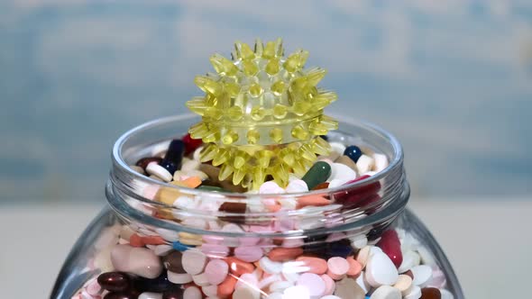 A large glass jar full of various pills rotates on a bluish background.