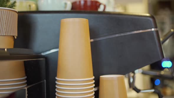 Brown Cardboard Coffee Cups Stacked in Each Other Next to a Professional Coffee Machine in the alt