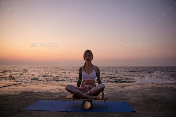Outdoor shot of young healthy female with good body shape posing over sea view during sunrise