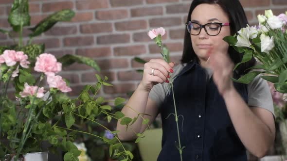 Florist girl in flower shop takes carnation out of vase and straightens petals alt