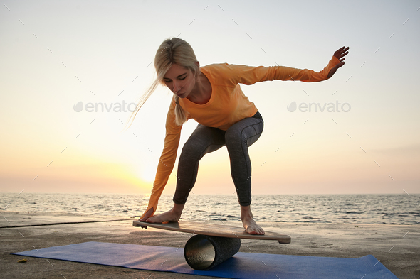 Outdoor shot of young lovely woman trying to keep balance on wooden desk, balancing