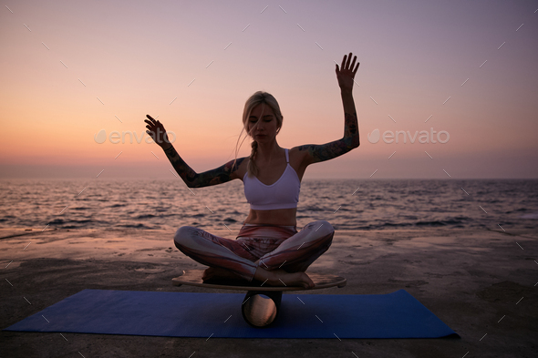 Outdoor shot of young healthy female with good body shape posing over sea view during sunrise